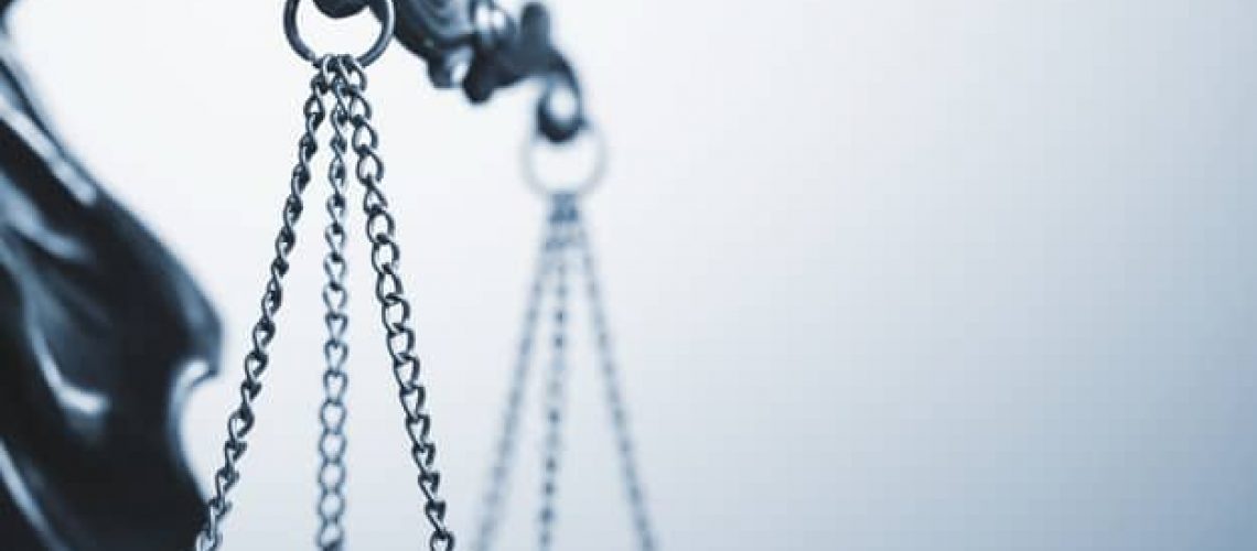Close up detail of the scales of justice being held aloft by a small statue of Justice over a grey background with copy space conceptual of law and order